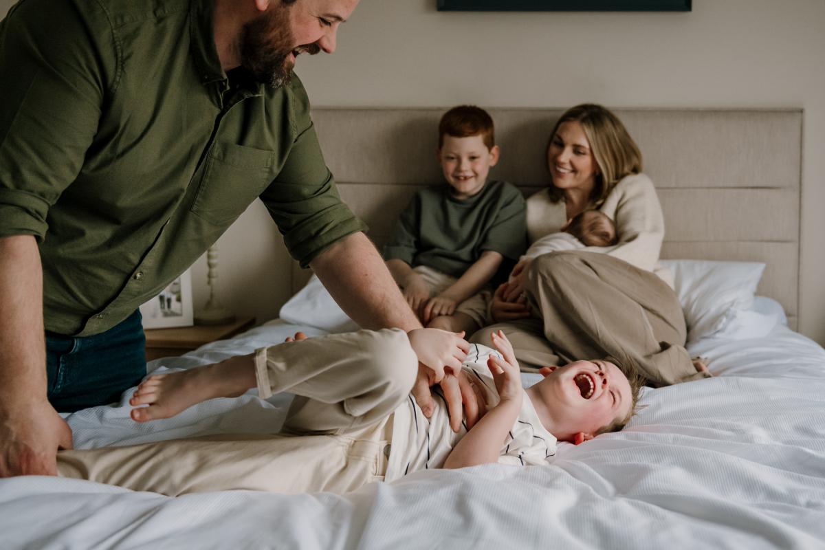 Dad tickling son on bed while family looks on